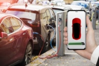Hand with phone on a background of electric car charging point. On a device screen indicator of power reserve.